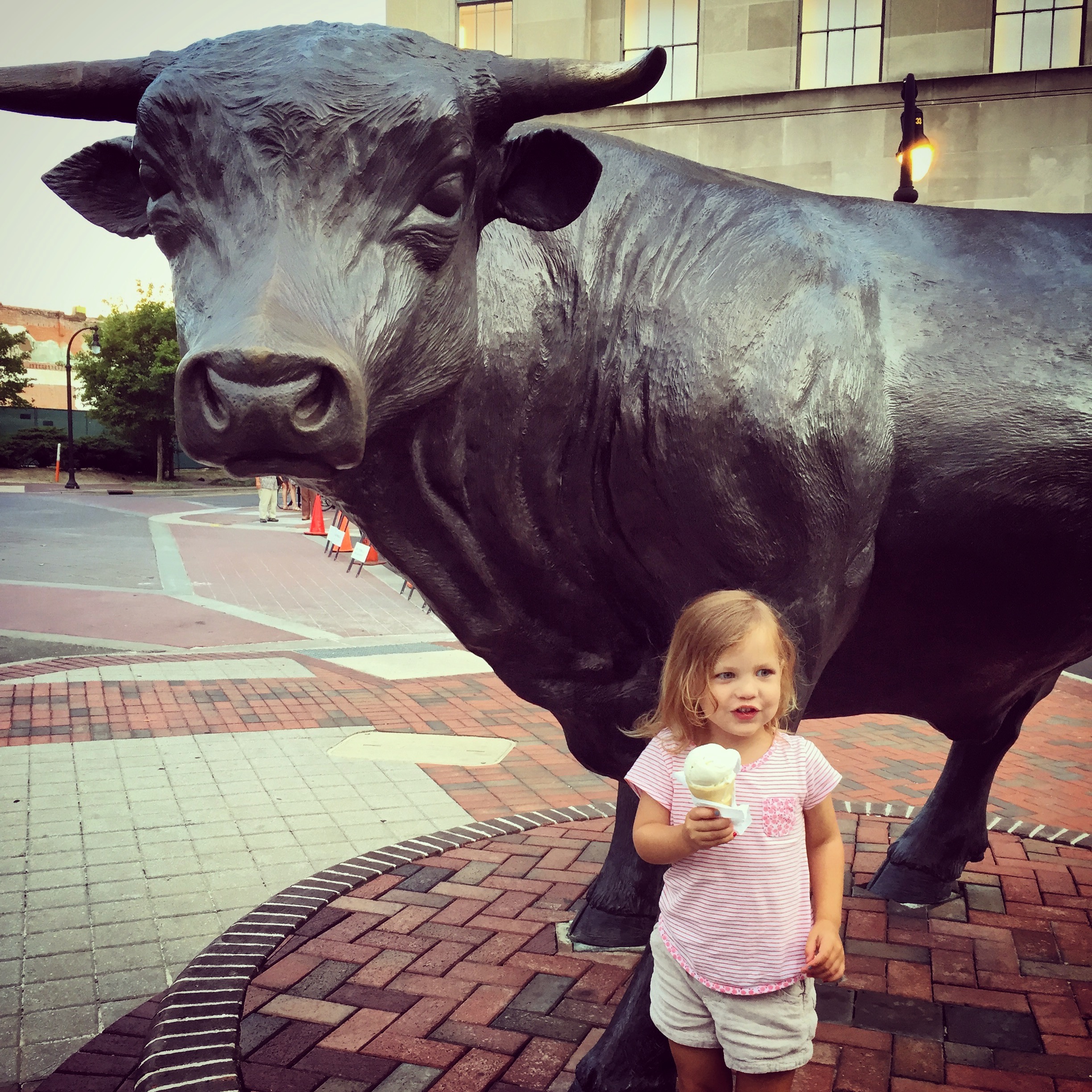 Little girl holding an ice cream cone in front of a large Durham bull statue, Major