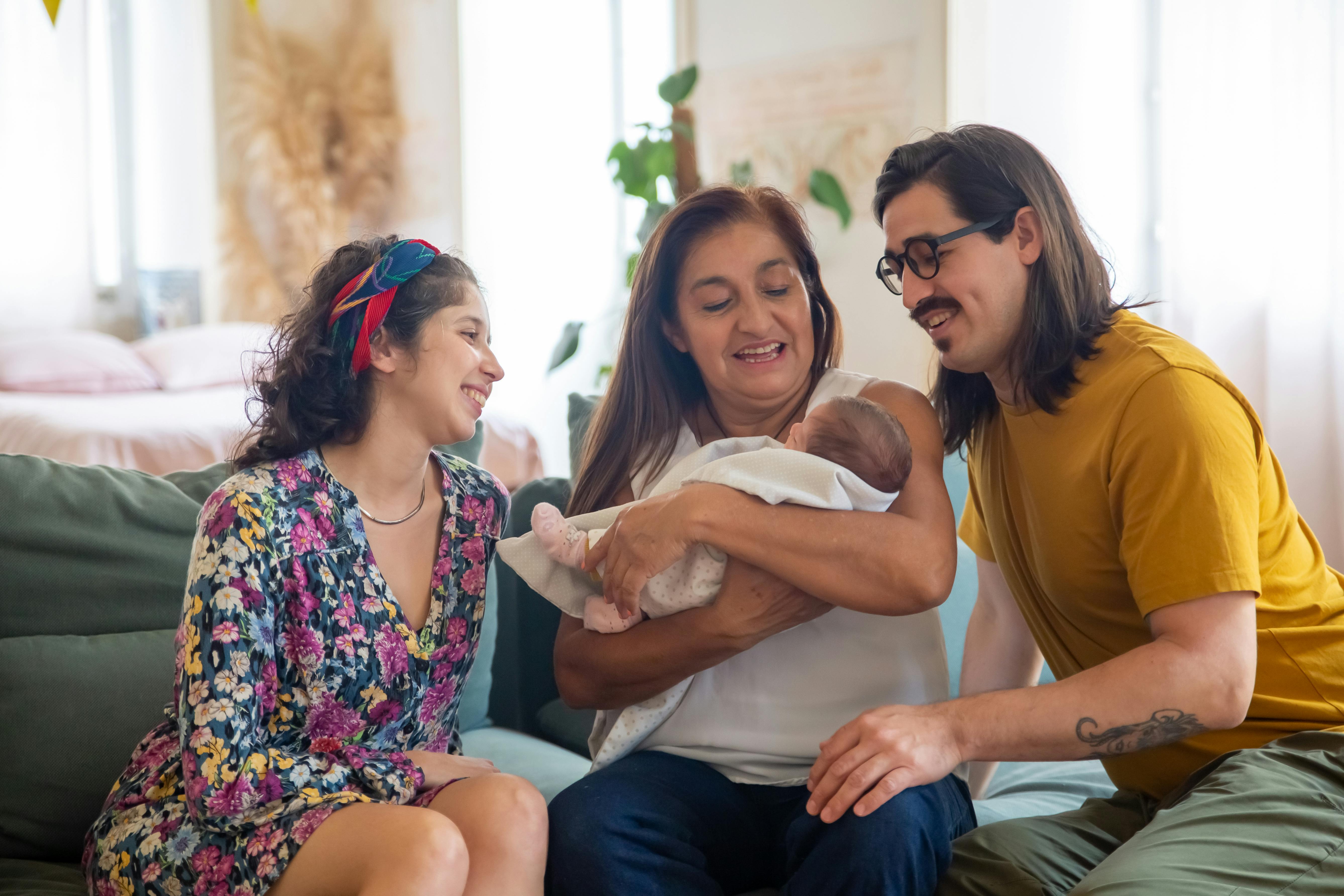 Family smiling while holding a newborn baby on a couch