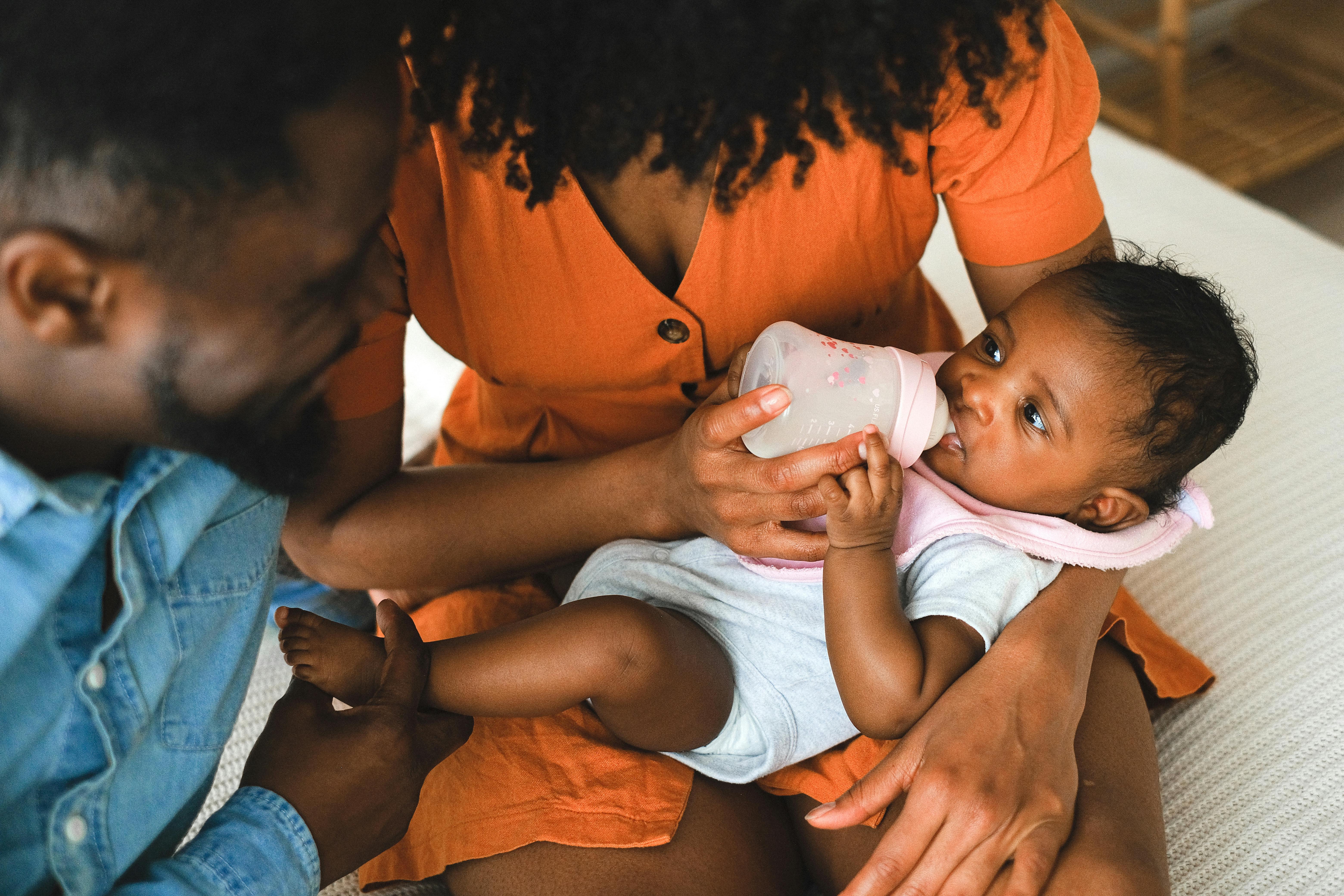 Mother in orange holding a baby, with a man leaning beside them.